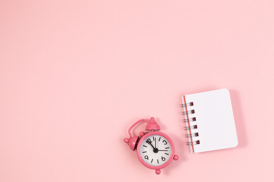 small alarm clock and clean notebook pastel pink background.