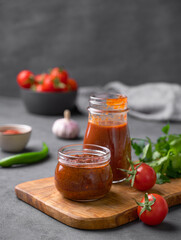 Tomato paste of hot pepper marinara with garlic, tomatoes and herbs in jars on a wooden board on a dark background.