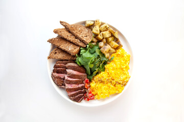Tenderloin beef steak with scrambled eggs, rocket leaves and potatoes with a side of rye bread.