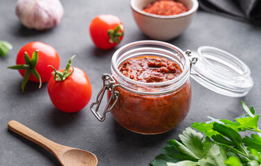 Homemade tomato sauce for pizza or pasta in a jar on a dark background with fresh vegetables, herbs and spicy close up.