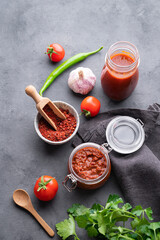 Homemade tomato sauce for pizza or pasta in a jar on a gray background with fresh vegetables, herbs and spicy.
