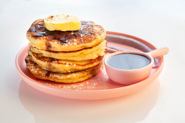 Stack of blue berry pancakes topped with honeycomb butter and maple syrup on a pink plate.