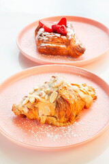Almond croissant placed on a pink plate with strawberry danish in the background.