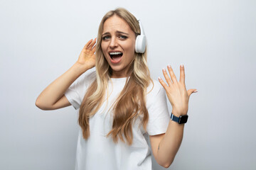 young woman sings along to music from headphones among white background