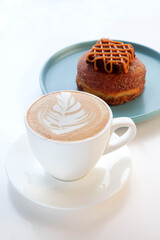 A cup of cappuccino coffee with chocolate brownie doughnut.