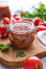 Homemade tomato sauce for pizza or pasta in a jar on a light background with fresh vegetables and herbs close up.