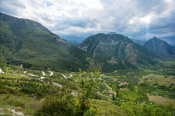 Landscape with mountains, road and fields with trees, flowers on a cloudy summer day after rain with a haze.