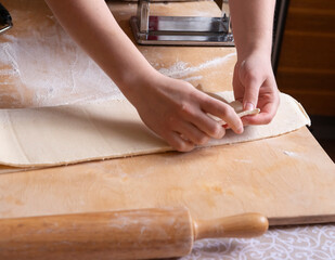 Close-up of the process of cooking homemade pasta. The chef prepares fresh traditional Italian pasta. Top view of the hands of a girl who is folding dough for further work. sfogliatelle in Neapolitan