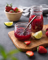 Two jars of strawberry jam on a wooden board on a dark background with fresh berries. Homemade sweets.