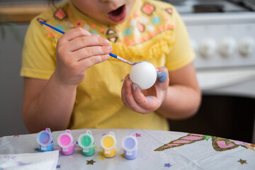 Child girl of preschool age painting Easter eggs at home kitchen. Easter spring traditions. Slow motion