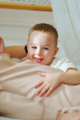 a cheerful cute little boy in a white T-shirt lies in bed 