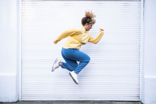 Carefree young woman jumping by white shutter