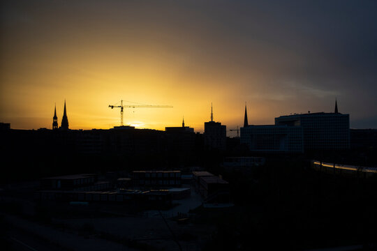Germany, Hamburg, Silhouettes of city spires and construction crane at sunset