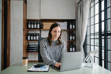 Confident business expert attractive smiling young woman typing laptop ang holding digital tablet  on desk in creative office.