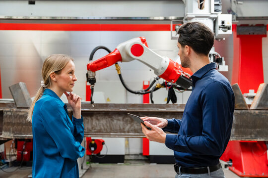 Mature engineer looking at technician holding tablet PC in robot factory