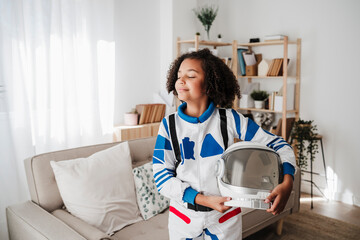 Smiling girl wearing space suit standing with eyes closed at home