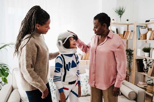 Mother and grandmother looking at granddaughter wearing space suit at home