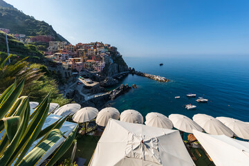 Italy, Liguria, Manarola, View of historic village alongCinqueTerre with row of beach umbrellas in foreground