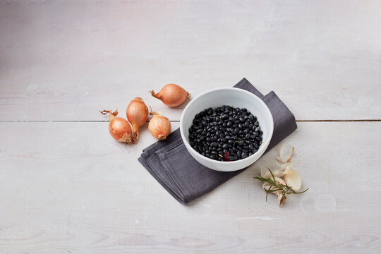 Studio shot of bowl of black beans, raw onions, garlic and rosemary