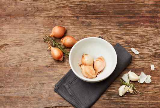 Studio shot of bowl, raw onions, garlic and rosemary