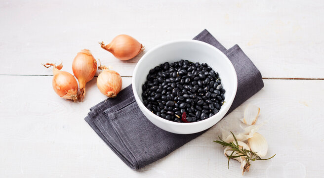 Studio shot of bowl of black beans, raw onions, garlic and rosemary