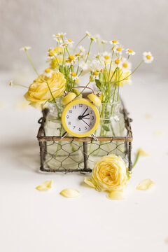 Yellow and white flowers in vase with alarm clock on table