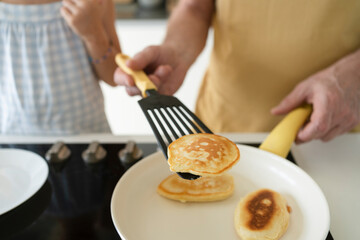 Hand of grandfather flipping pancake using spatula in kitchen at home