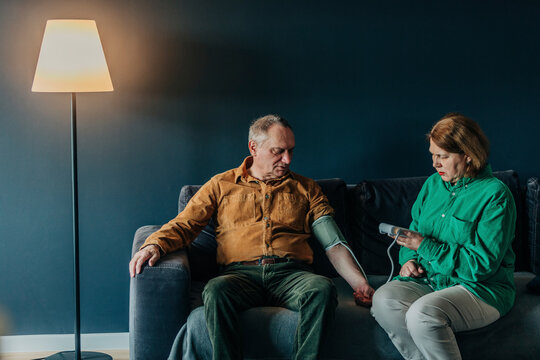 Senior woman checking blood pressure of man sitting on sofa at home