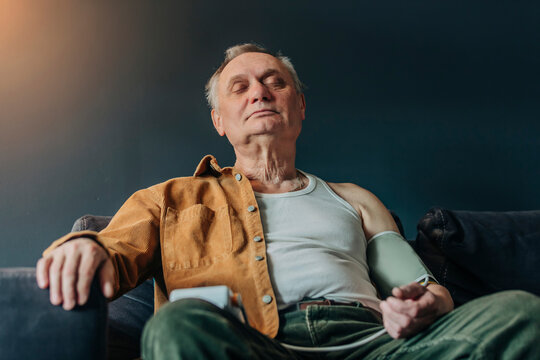 Senior man with eyes closed checking blood pressure sitting on sofa