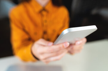 close-up, young woman's hand holding a smartphone and typing a message. Concept of working from home, shopping online, sending email, playing phone