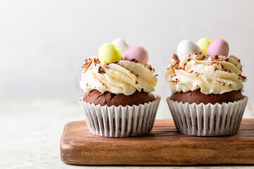 Easter chocolate cupcakes with cream cheese, sweet candy eggs and nest. Holiday homemade dessert. Close-up.
