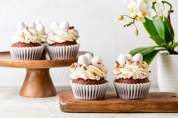 Easter table with chocolate muffins or cupcakes, sweet candy eggs and cream cheese nest. Spring white flowers. Holiday homemade dessert.