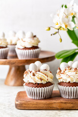 Obraz na płótnie Canvas Chocolate cupcakes with sweet candy eggs and cream cheese nest. Holiday or Easter homemade dessert. Spring flowers. Light background, vertical image.