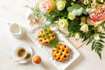Obraz na płótnie Canvas Flowers on the romantic breakfast table. Selective focus. Blured mini tartlet or pies crust with berries. Espresso coffee cup, hard boiled egg, water, flowers. Directly above.