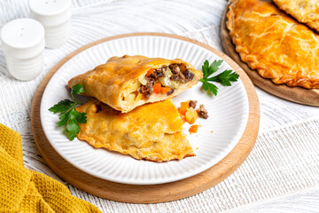 Baked meat turnovers or pies, or empanadas, or cornish pasty with filling, beef, carrot, and potato, white plate.