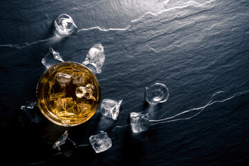 Glass of whiskey with ice cubes on dark table