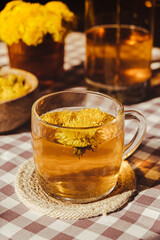 Dandelion flower healthy tea in glass teapot and glass cup on table. Delicious herbal Hot tea from fresh dandelion flowers at home at summer day. Green clearing. Bouquet of dandelions petals