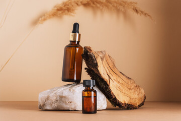 Brown cosmetic serum and essential oil bottles on a stone podium and wooden bark, pampas grass...