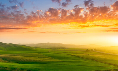 countryside sunset in green hills of spring fields with old castle farm and mountains on background of evening landscape