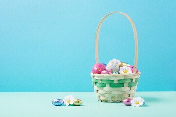 Fototapeta na wymiar Easter Basket, Sweet Colorful Chocolate Easter Eggs, Daisy Flowers on Pastel Blue Mint Background.