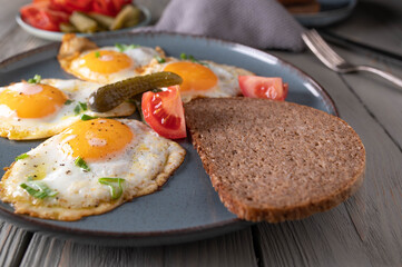 Fried eggs, sunny side up with rye bread, tomatoes and pickles. Traditional german, rustic meal