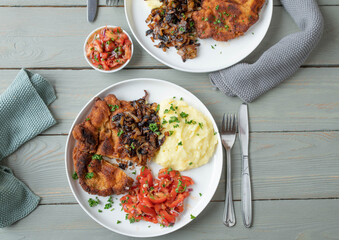 Breaded cutlet with roasted onions, mashed potatoes and tomato salad on a plate