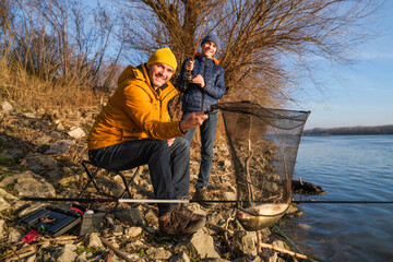 Father and son are fishing on sunny winter day. They caught a fish and are holding it in a landing net.