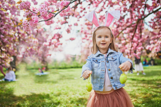 Preschooler girl wearing bunny ears playing egg hunt on Easter