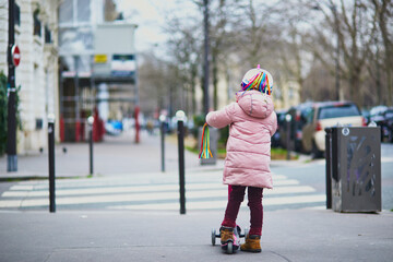 Adorable preschooler girl riding her scooter on a street of Paris, France