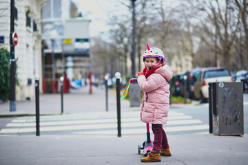 Adorable preschooler girl riding her scooter on a street of Paris, France