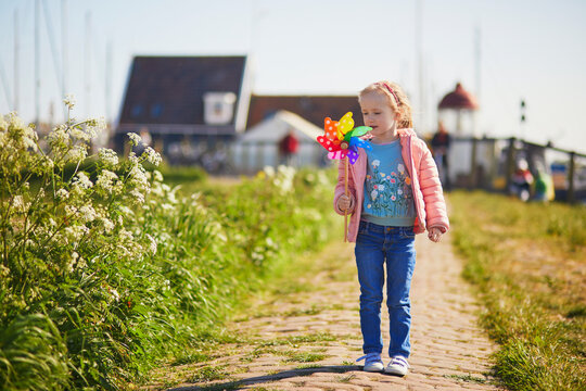 Adorable preschooler girl with colorful pinwheel walking in picturesque village of Marken, North Holland, the Netherlands