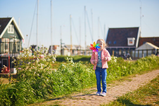 Adorable preschooler girl with colorful pinwheel walking in picturesque village of Marken, North Holland, the Netherlands