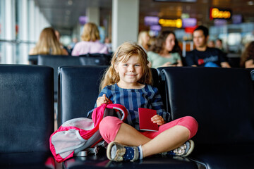 Little girl at the airport waiting for boarding at the big window. Cute kid holding passport..Looking forward to leaving for a family summer vacation