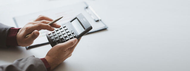Businessman using a calculator to calculate numbers on a company's financial documents, he is analyzing historical financial data to plan how to grow the company. Financial concept. - obrazy, fototapety, plakaty